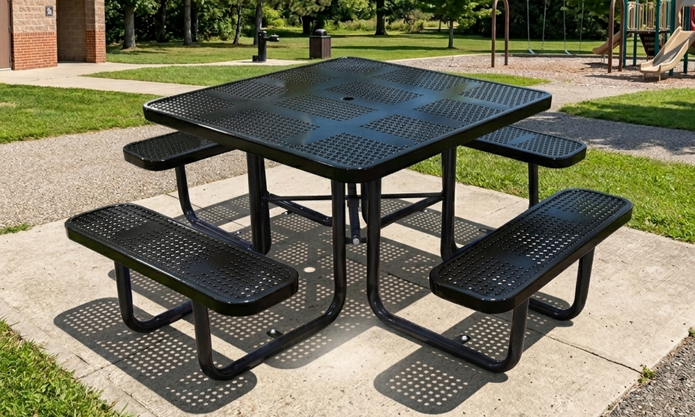 Black perforated steel picnic table with surface mount legs installed on concrete at a commercial playground and park setting